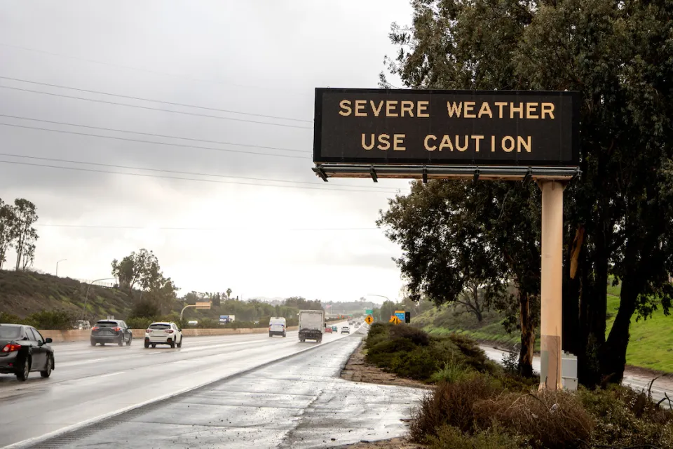 Freeway sign with "severe weather - use caution" over multilane freeway in rainy weather.